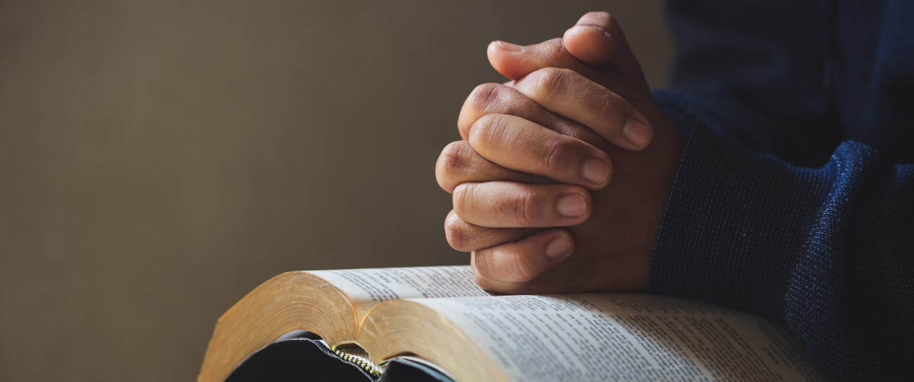 Hands clasped in prayer over Bible